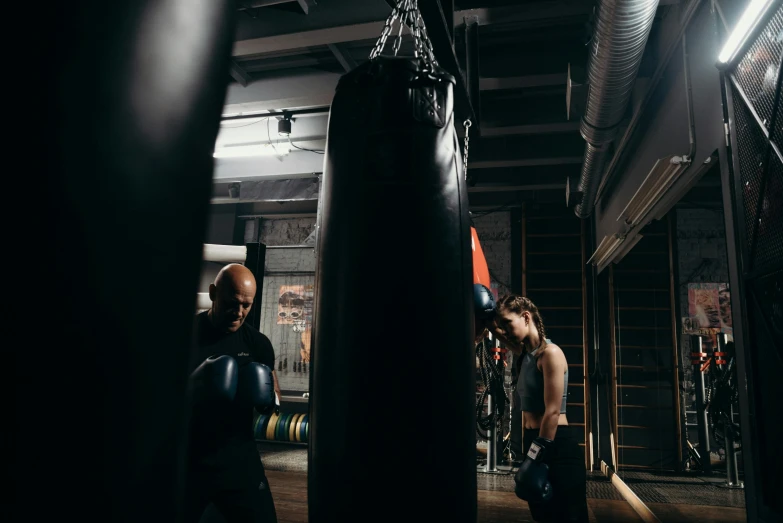 a man standing next to a punching bag, by Emma Andijewska, pexels contest winner, figuration libre, medium shot of two characters, working out, inside a grand, te pae