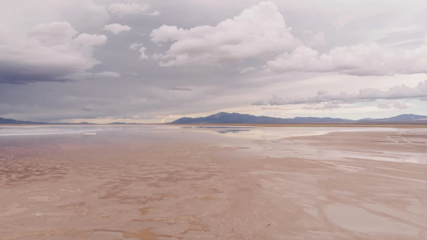 a man riding a surfboard on top of a sandy beach, inspired by Benjamin Williams Leader, unsplash contest winner, land art, pink and grey clouds, utah, a photo of a lake on a sunny day, sparse mountains on the horizon