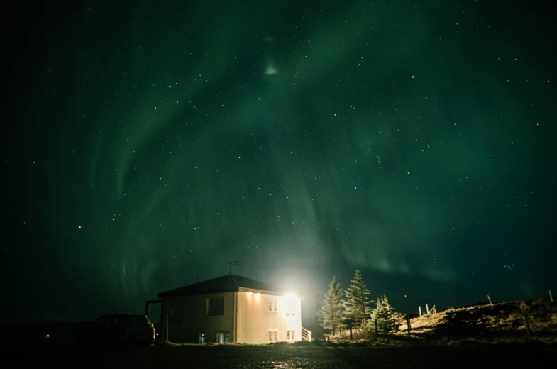 a person standing in front of a building under the aurora lights, by Sebastian Spreng, unsplash contest winner, light and space, pale green glow, remote icelandic village, at night with moon light, lines of lights