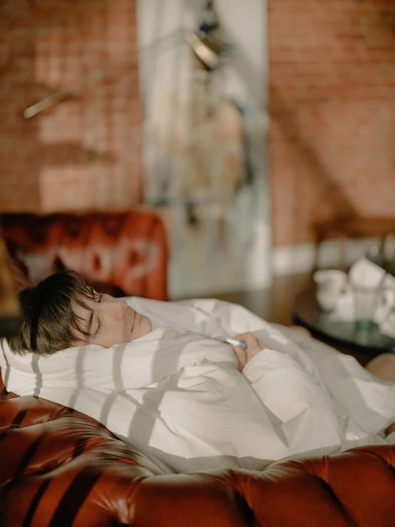 a man laying on top of a brown leather couch, inspired by Elsa Bleda, pexels contest winner, wearing white robe, profile image, white bed, covered with blanket