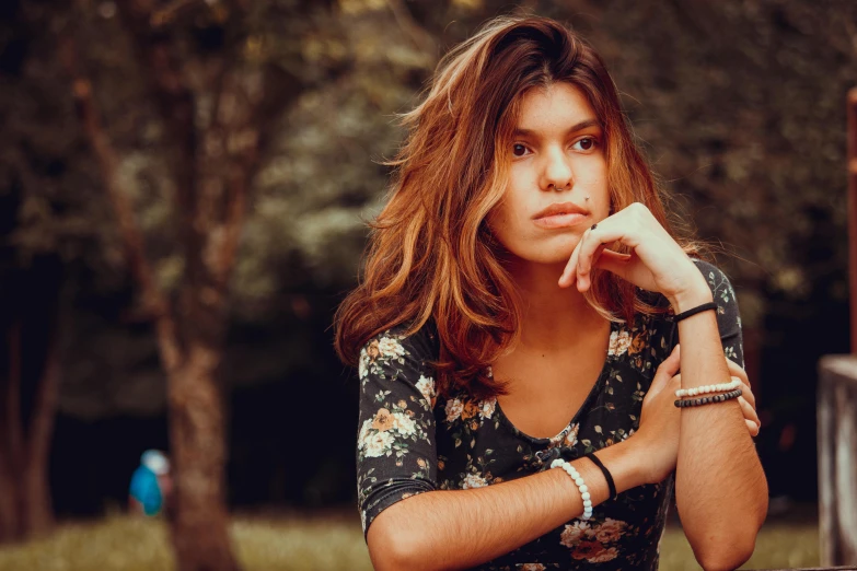 a woman sitting at a table with her hand on her chin, trending on pexels, in the park, brown haired, teenage, grungy woman