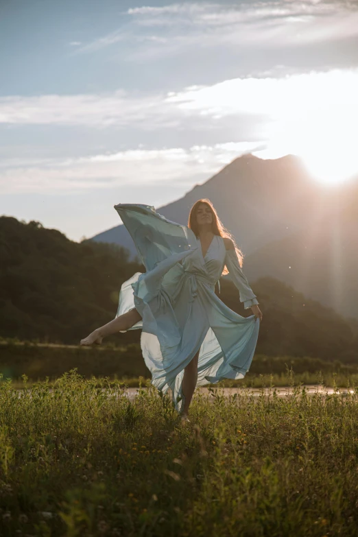 a woman standing on top of a lush green field, arabesque, modern dance aesthetic, sunset in a valley, wearing silver silk robe, portrait featured on unsplash