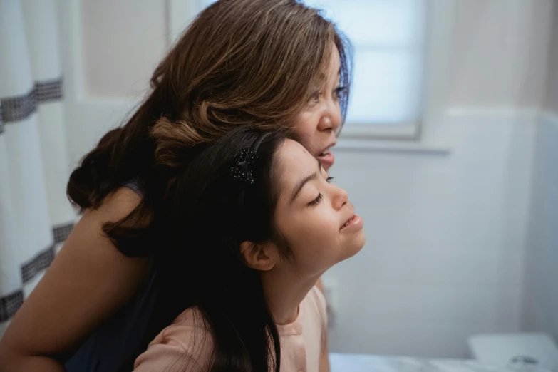 a woman sitting on top of a bed next to a woman, pexels contest winner, young asian girl, profile image, motherly, head tilted down