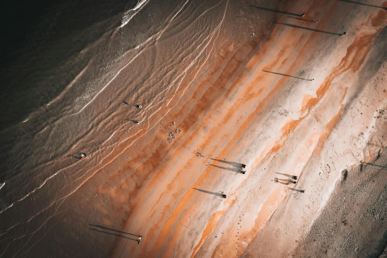 a group of boats sitting on top of a sandy beach, a microscopic photo, inspired by Andreas Gursky, unsplash contest winner, land art, gray and orange colours, streaks, people in beach, “ iron bark