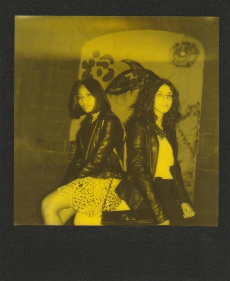 a couple of women sitting next to each other, a polaroid photo, unsplash, international gothic, black and yellow, she wears leather jacket, phosphorescent, asian descend