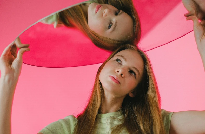 two women standing next to each other in front of a mirror, an album cover, by Anna Füssli, pexels contest winner, sadie sink, pink and red color scheme, panoramic view of girl, young woman looking up