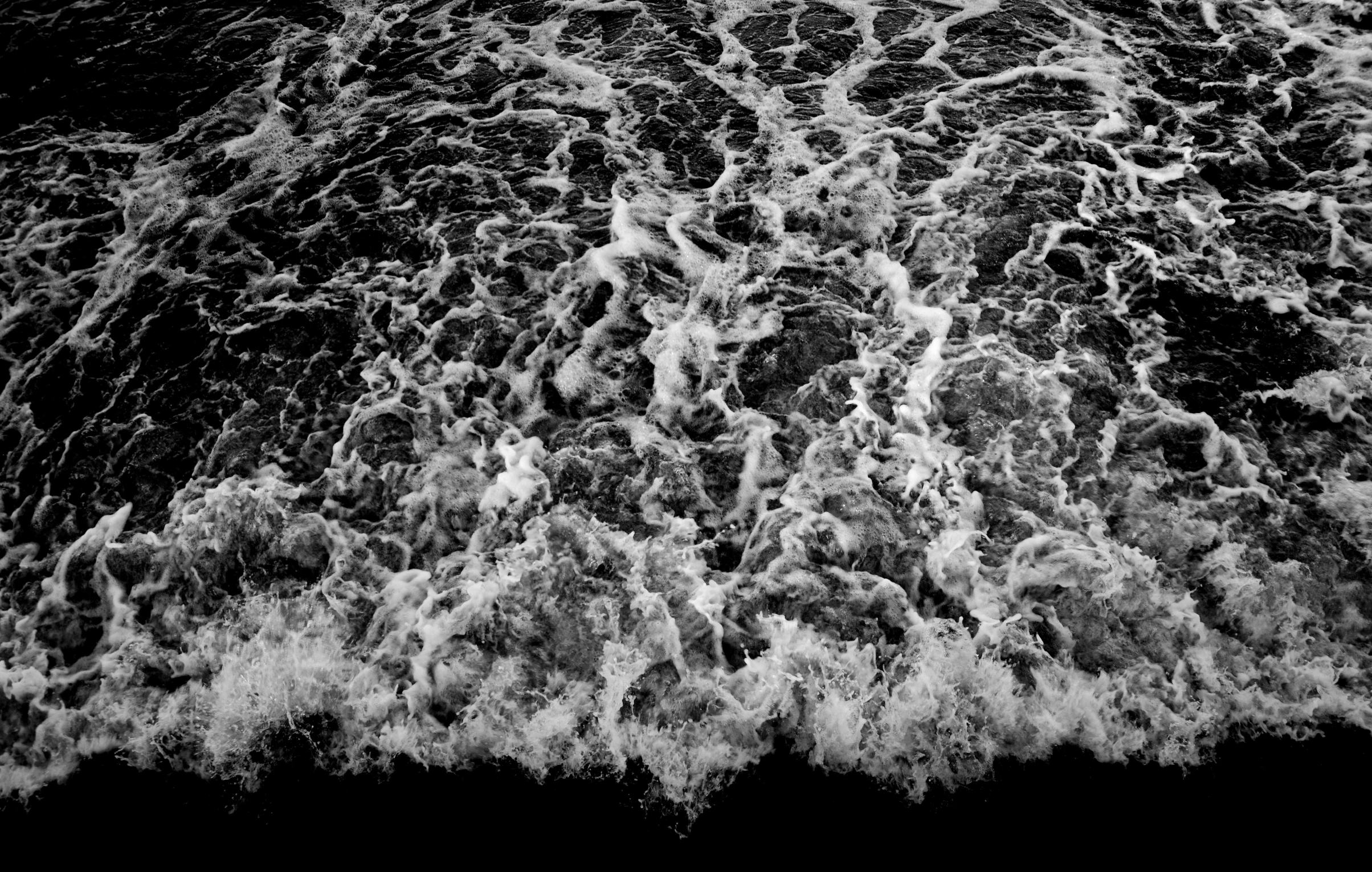 a black and white photo of a body of water, by Thomas Fogarty, conceptual art, extremely detailed water texture, waves and splashes, top down perspecrive, ocean pattern and night sky
