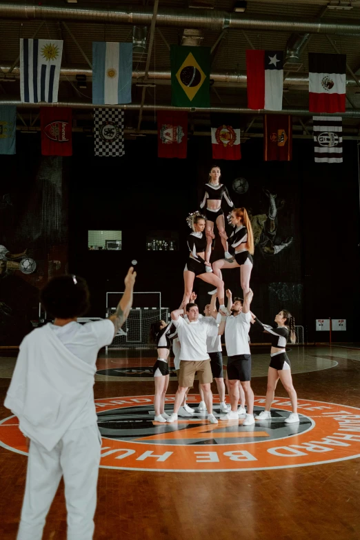 a group of people standing on top of a basketball court, acrobatic moveset, orange and white, tall ceiling, pyramid