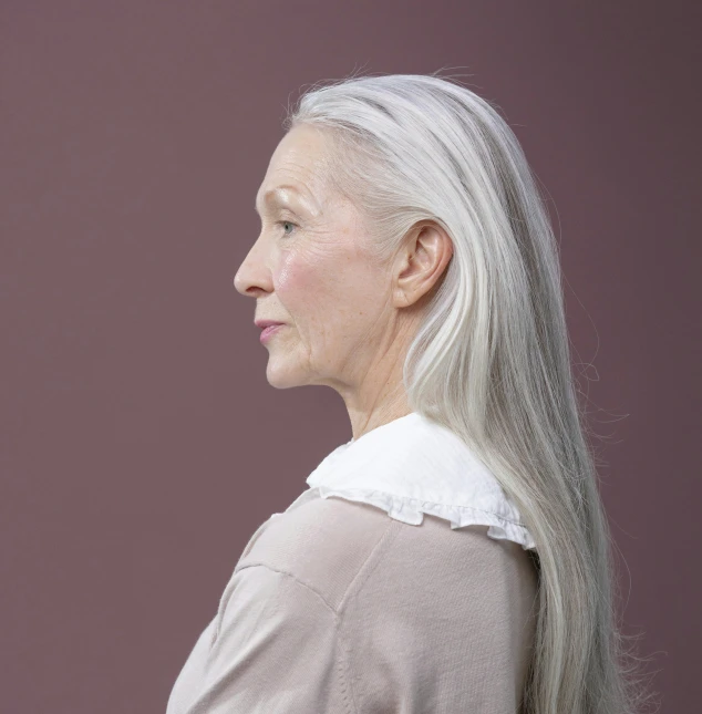 a woman with long white hair standing in front of a purple wall, by Gavin Hamilton, side profile view, aging, grey ears, plain background