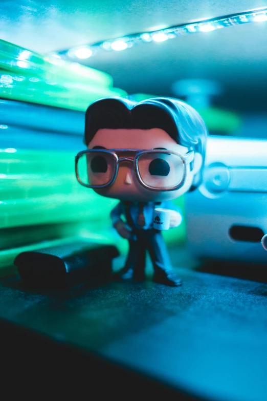 a close up of a toy with a car in the background, by Ryan Pancoast, unsplash, holography, portrait of hank hill, zach galifianakis funko pop, wide angle lens glow in the dark, gamer screen on metallic desk