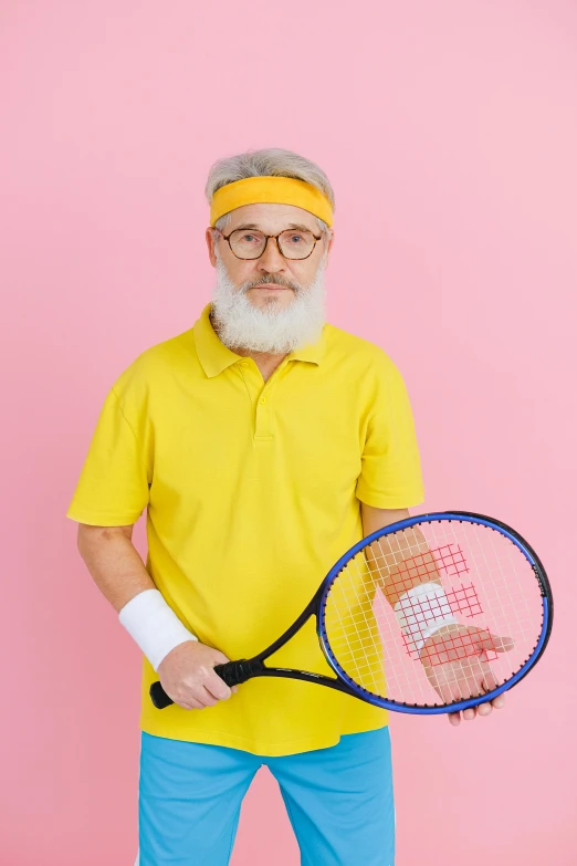 a man in a yellow shirt and blue pants holding a tennis racket, white hair and white beard, wearing a pink head band, 2019 trending photo, healthcare