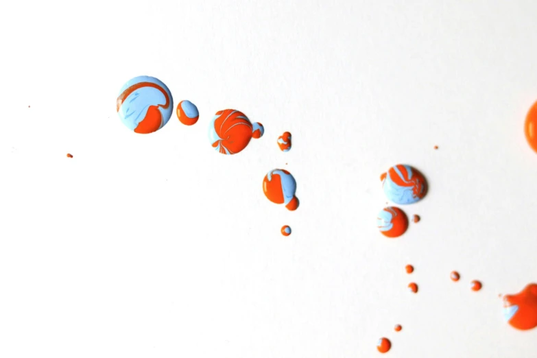 a group of buttons sitting on top of a white surface, a detailed painting, inspired by Alexander Calder, orange and cyan paint decals, detailed droplets, studio product shot, pouring