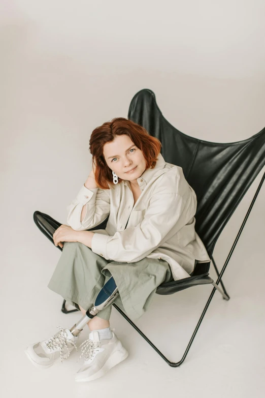 a woman sitting in a black butterfly chair, by Grytė Pintukaitė, trending on unsplash, renaissance, in front of white back drop, sadie sink, 40 years old women, leather robes