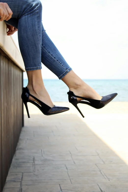 a woman sitting on a wall wearing high heels, pexels, blue-black, patent style, standing near the beach, instagram post