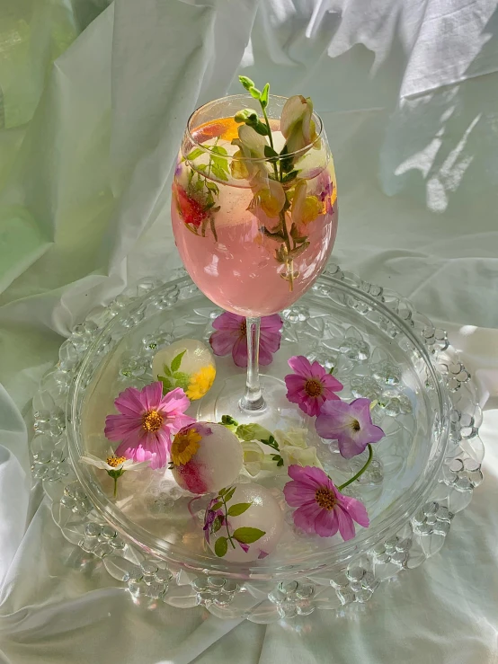 a pink drink sitting on top of a glass plate, with frozen flowers around her, taken on iphone 14 pro, edible flowers, jelly - like texture. photograph