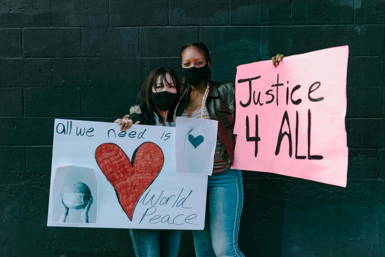 a couple of women standing next to each other holding signs, a photo, by Julia Pishtar, trending on unsplash, black arts movement, masked heroes, world peace, 3 4 5 3 1, illustration:.4