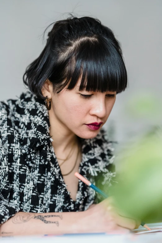 a woman sitting at a table writing on a piece of paper, inspired by Ruth Jên, visual art, black hair and white bangs, next to a plant, concentrated look, full close-up portrait