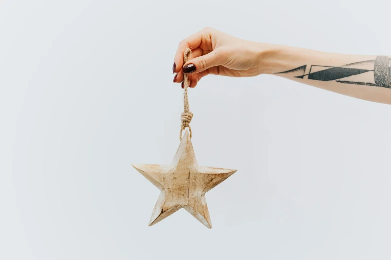 a person holding a wooden star ornament, by Emma Andijewska, trending on pexels, in a white boho style studio, viewed from the side, unsplash transparent, hero prop