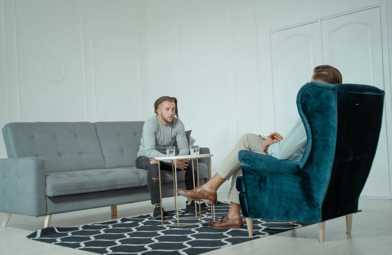 a man and a woman sitting on a couch in a living room, inspired by Constantin Hansen, pexels contest winner, hurufiyya, in a meeting room, blue and gray colors, complaints, people on the ground