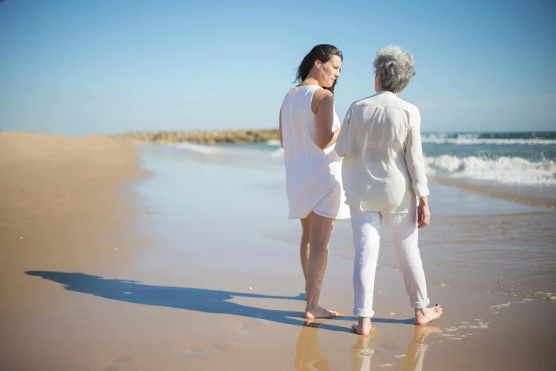 a couple of women standing on top of a sandy beach, an elderly, profile image, australian beach, a woman walking