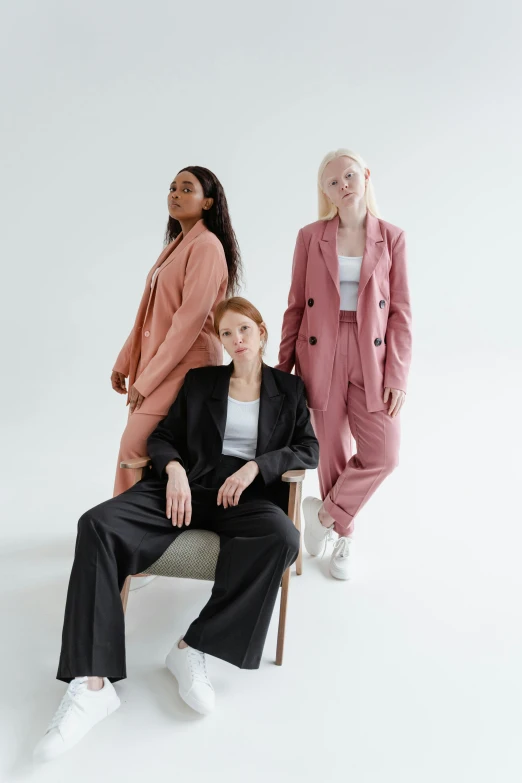 three women sitting on a chair in front of a white background, trending on pexels, wearing a light - pink suit, creterion collection, wearing causal black suits, muted colors. ue 5