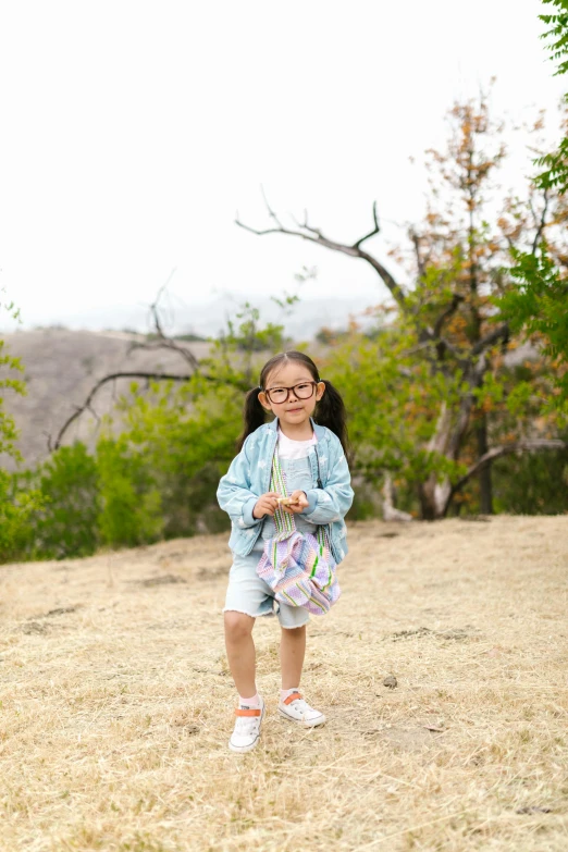 a little girl that is standing in the grass, a picture, inspired by Hikari Shimoda, unsplash, malibu canyon, view(full body + zoomed out), wearing medium - sized glasses, on the mountain