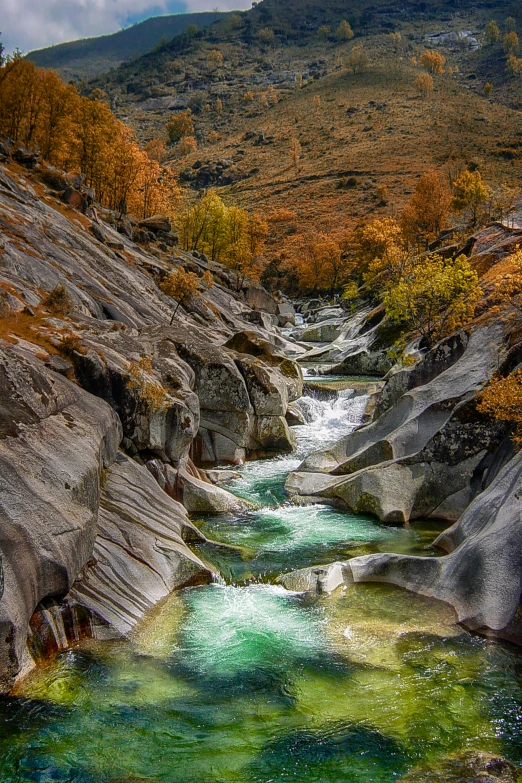 a river running through a lush green valley, by Franz Hegi, autumnal colours, crazy looking rocks, glacier, rock pools