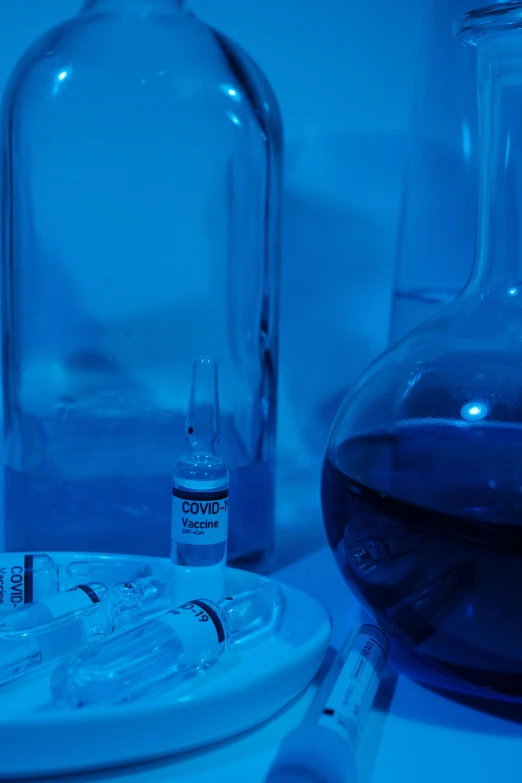 a glass bottle sitting on top of a table next to a plate, a picture, holding syringe, purple and blue neons, thumbnail, in a lab