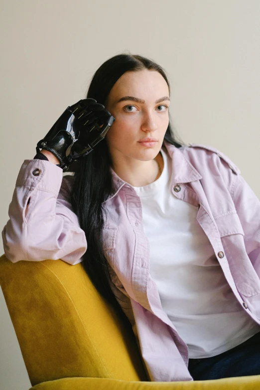 a woman sitting on top of a yellow chair, an album cover, trending on pexels, black leahter gloves, wearing a pastel pink hoodie, kate bishop, wearing a white button up shirt