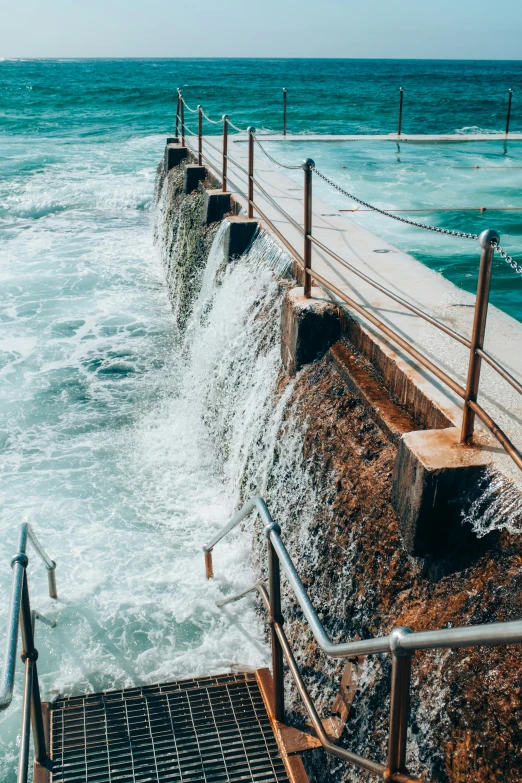 a man standing on top of a pier next to the ocean, trending on pexels, happening, sewage falling from grates, small flowing stream from wall, manly, pools