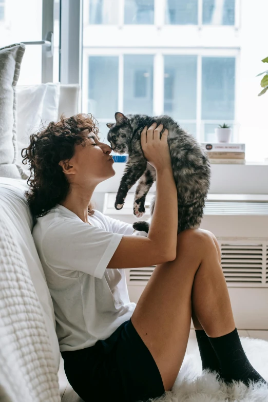 a woman sitting on a couch holding a cat, pexels contest winner, brown curly hair, smelling good, gif, natural light in room