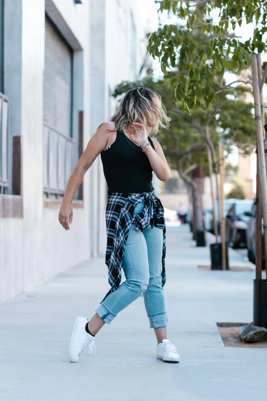 a woman walking down a sidewalk talking on a cell phone, doing a sassy pose, flannel, wearing a cropped black tank top, wearing ragged clothing