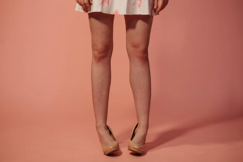 a woman standing in front of a pink background, by Elsa Bleda, beautiful legs, wearing honey - themed miniskirt, very pale skin, swollen veins