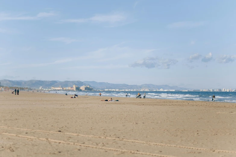 a group of people standing on top of a sandy beach, tocchini, from the distance, albert ramon puig, skyline in the distance