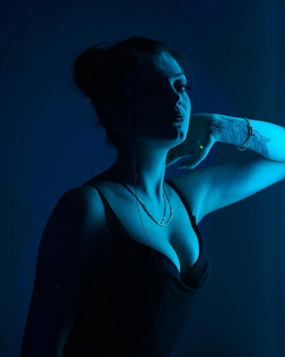 a woman with a tattoo on her arm, an album cover, inspired by Elsa Bleda, unsplash, art photography, blue neon, bisexual lighting, profile image, standing in a dimly lit room