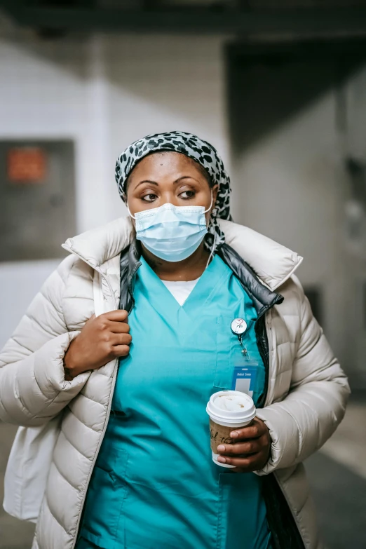 a woman wearing a face mask and holding a cup of coffee, by Jason Felix, happening, nurse scrubs, walking towards the camera, african woman, er drama