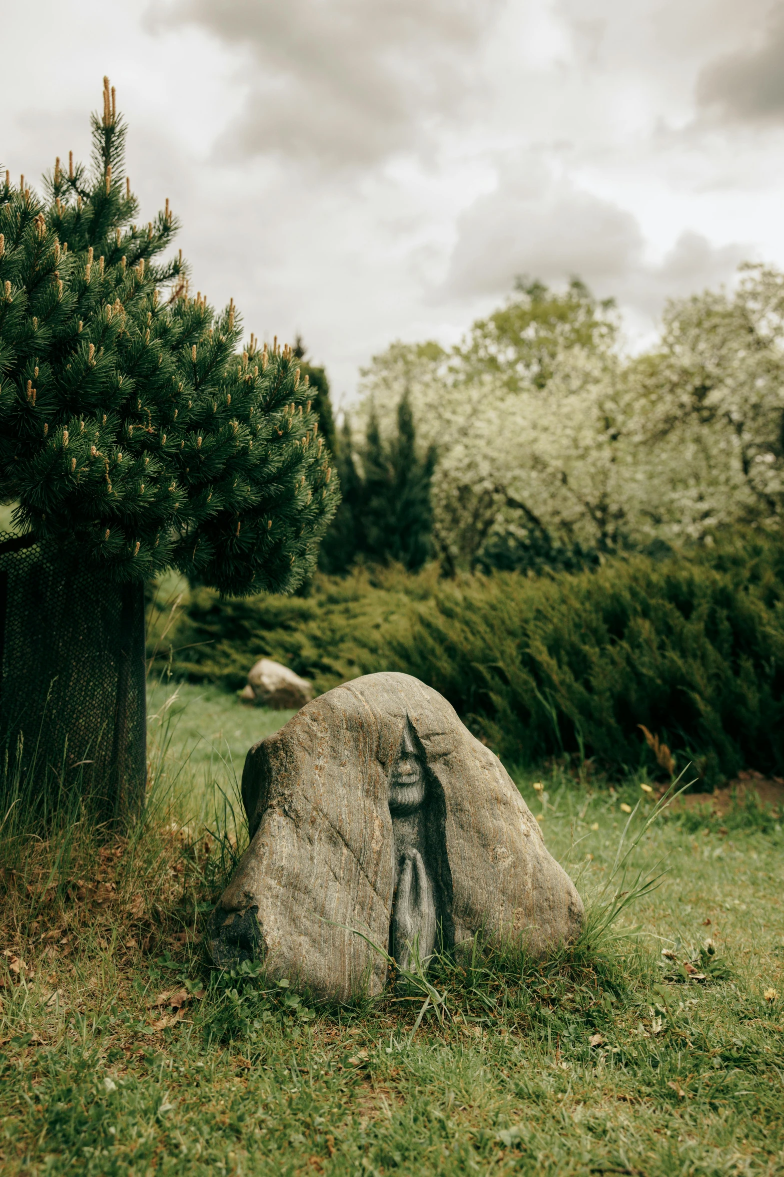 a large rock sitting on top of a lush green field, a statue, by Jesper Knudsen, unsplash, land art, in a garden, tombstone, miniature forest, slight overcast