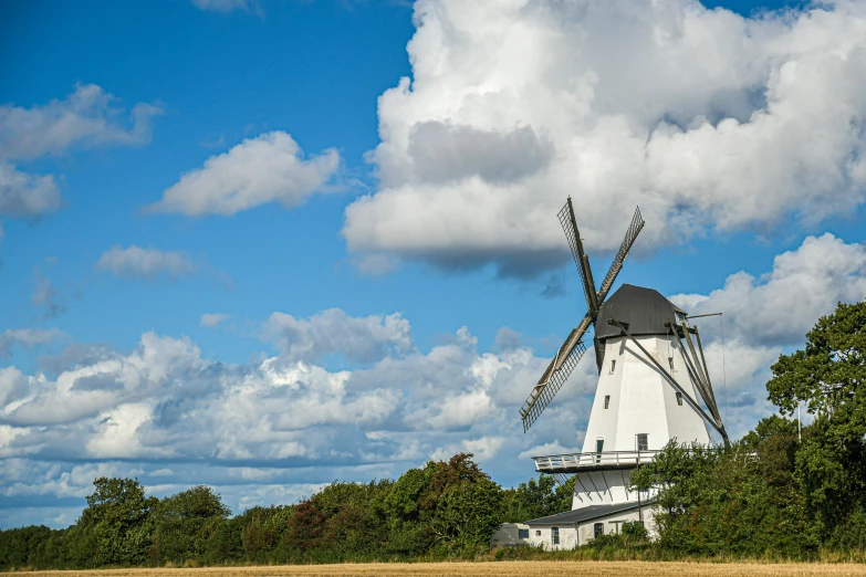a windmill sitting in the middle of a field, by Jesper Knudsen, blue skies, historical setting, large white clouds, exterior photo