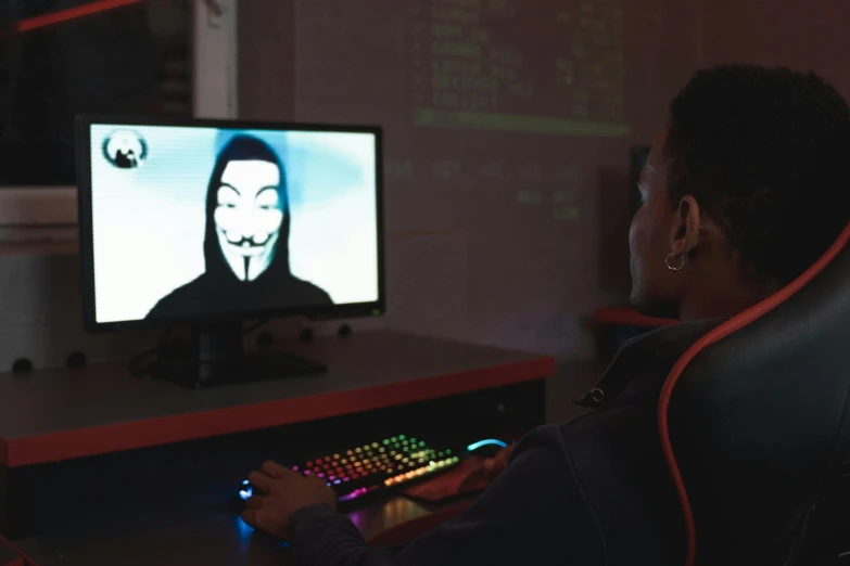 a person sitting in a chair in front of a computer, anonymous mask, a teen black cyborg, gaming room, hackerman