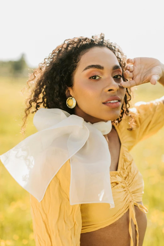 a woman standing in a field of yellow flowers, a portrait, trending on pexels, renaissance, lacey accessories, tessa thompson inspired, white scarf, wide ribbons