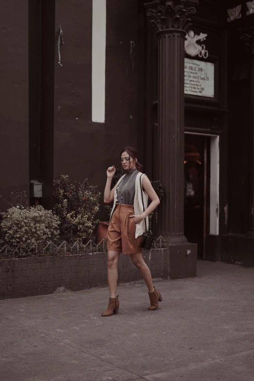 a woman walking down a sidewalk talking on a cell phone, by Cherryl Fountain, unsplash, renaissance, muted browns, wearing a camisole and shorts, jakarta, fashion pose