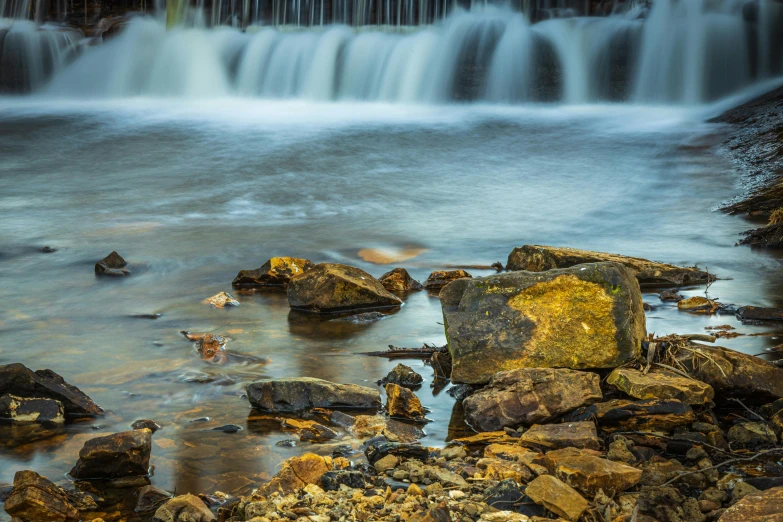 a waterfall flowing over rocks into a body of water, a picture, unsplash contest winner, old lumber mill remains, medium format. soft light, esher, 4k photo”