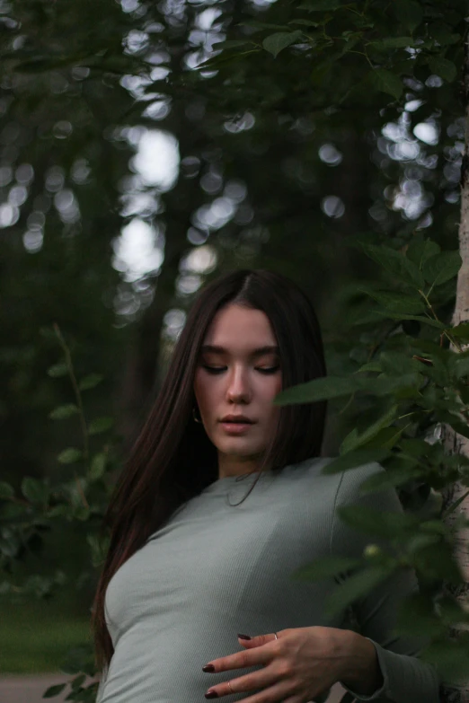 a pregnant woman standing next to a tree, an album cover, inspired by Elsa Bleda, unsplash contest winner, young woman with long dark hair, sad look, green clothes, hailee steinfeld