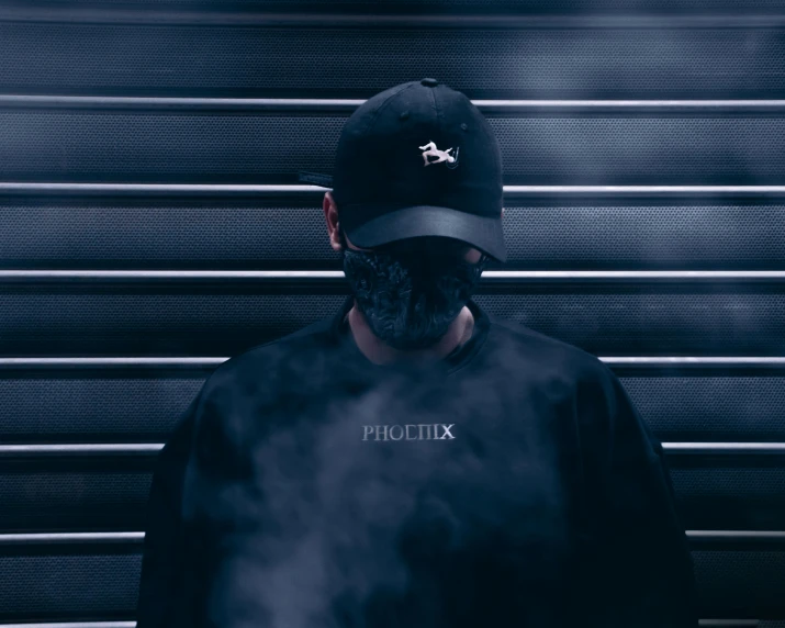 a man wearing a black hat and a black shirt, an album cover, pexels contest winner, techwear clothes, phoenix head, volumetrig fog, security rhox
