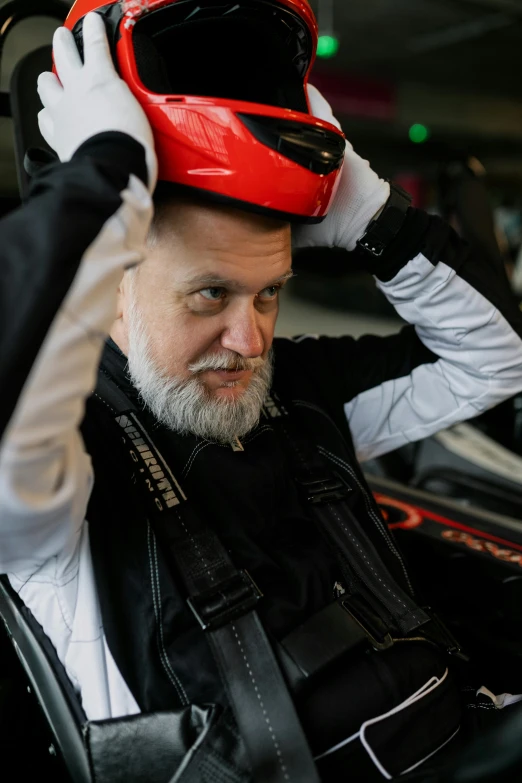 a man sitting in a car with a helmet on his head, inspired by Graham Forsythe, full white beard, bending down slightly, looking confident, mechanics