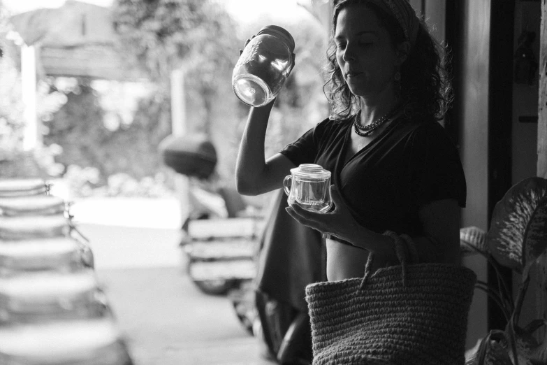 a black and white photo of a woman drinking from a cup, by Daniel Lieske, unsplash, holding mesh bag with bagels, jars, porches, 30-year-old woman from cuba