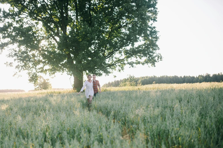 a man and a woman walking through a field, by Jakob Häne, unsplash, laying under a tree on a farm, summer evening, low quality photo, medium format. soft light