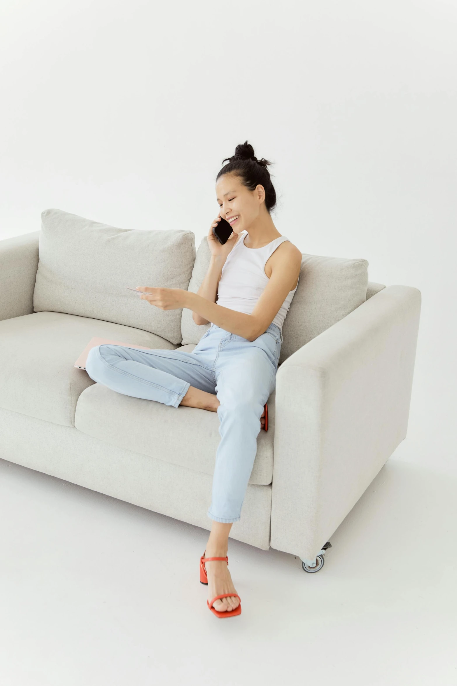 a woman sitting on a couch talking on a cell phone, wearing off - white style, wearing jeans, on a white table, no text!