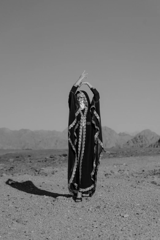 a woman standing in the middle of a desert, a black and white photo, arabesque, waving robe movement, official music video, on a mountain, deity)