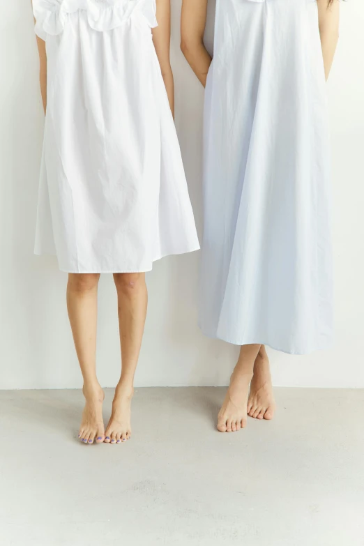 a couple of women standing next to each other, by Eizan Kikukawa, unsplash, minimalism, wearing a nightgown, close-up on legs, white and pale blue, cotton fabric